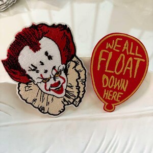 May include: Embroidered patches featuring a scary clown face with red hair and a ruffled collar. A red balloon-shaped patch with the text "WE ALL FLOAT DOWN HERE" in gold lettering is also included.