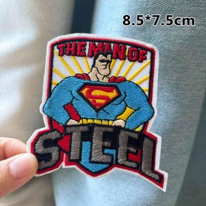 Puede incluir: Parche bordado con Superman en una pose clásica. El parche es azul, rojo, amarillo y blanco, con el texto "THE MAN OF STEEL". Mide 8,5 x 7,5 cm.