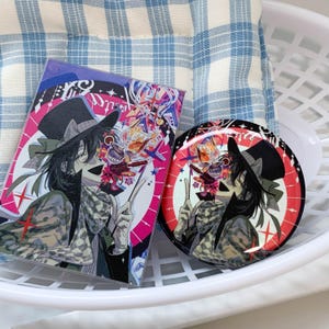 May include: A rectangular acrylic standee and a circular pin button featuring an anime-style character wearing a black top hat and a checkered scarf. The character has dark hair and is surrounded by colorful abstract shapes, stars, and drink icons.