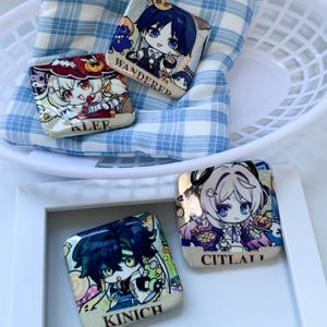 Może przedstawiać: Cztery kwadratowe przypinki z ilustracjami postaci w stylu anime. Przypinki zawierają napisy KLEE, WANDERER, KINICH oraz CITLALI czarną czcionką. Każda przypinka ma błyszczące, brokatowe wykończenie z kolorowymi grafikami przedstawiającymi postacie.