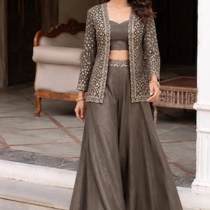 May include: A three-piece set in a dark taupe shade consisting of a sleeveless crop top, wide-leg palazzo pants with a high waistband, and a long-sleeved open jacket. The jacket features a detailed metallic gold floral pattern along the front edges.