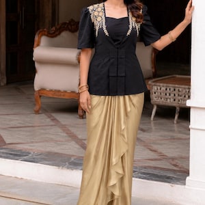 May include: A black short-sleeved top featuring gold floral embroidery on the shoulders and a structured peplum waist, paired with a floor-length metallic gold skirt that has a draped front panel with cascading ruffles and a high-low hemline.
