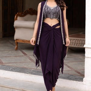 May include: A dark purple three-piece ensemble consisting of a sleeveless vest with silver embroidered trim, a cropped sleeveless top with silver sequin and bead embellishments, and a matching draped dhoti-style skirt with a knotted waist detail.
