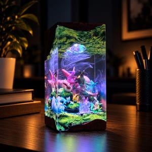 May include: A rectangular resin lamp featuring a dark wood base and top, enclosing a miniature diorama of multiple colorful creature figurines nestled in green mossy terrain, illuminated by internal blue and purple LED lights.