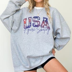 Light gray USA Figure Skating sweatshirt with patriotic red white blue skater silhouettes, cozy oversized crewneck for skating moms, winter competition fan apparel, ice skating gift for women.