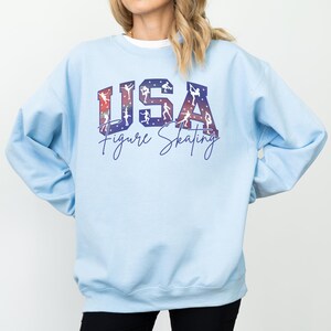 Light blue USA Figure Skating sweatshirt with red white blue skater silhouettes, cozy oversized skating mom crewneck, patriotic ice skating fan apparel, winter sports gift.