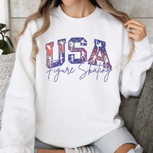 White USA Figure Skating sweatshirt with patriotic skater silhouettes, cozy winter sports crewneck for skating moms, team competition outfit, ice skating fan apparel.