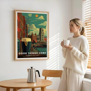 May include: A framed art print featuring a stylized illustration of a city scene with a large pint of stout. The artwork includes the text "GOOD THINGS COME - TO THOSE WHO WAIT". The print is in a light wood frame.