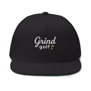 Puede incluir: Gorra negra de ala plana con la inscripción bordada "Grind golf" en escritura blanca. Una pequeña bandera de golf amarilla está bordada junto a la palabra "golf". La gorra tiene una parte inferior verde.