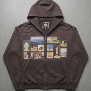 May include: A brown zip-up hoodie with a hood and a star logo on the chest. The front of the hoodie features a collage of framed images. The images include a skull, landscapes, and figures.