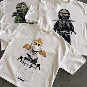 May include: White t-shirts with graphic illustrations of ninja characters in various colors. The ninja figures are depicted in a block-style design. One shirt has the text "(INHUMAN) ゼーン" printed on it.