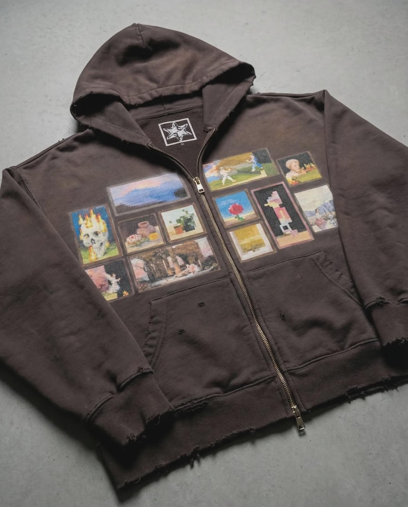 May include: Brown zip-up hoodie with a distressed finish. The front of the hoodie is adorned with a series of small, colourful framed images. These include a skull, landscapes, and other illustrations. The hoodie has a hood and a metal zip.