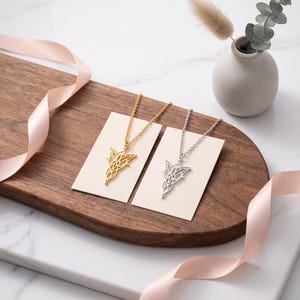 May include: Two necklaces, one gold-toned and one silver-toned, each featuring an intricate, symmetrical, openwork pendant with a pointed, leaf-like design. The necklaces are displayed on individual white rectangular cards.