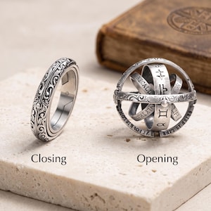 May include: A silver-toned astronomical ring shown in two states: a closed band with intricate scrollwork and an opened sphere featuring engraved zodiac symbols, text, and celestial markings. The text "Closing" and "Opening" is printed below.