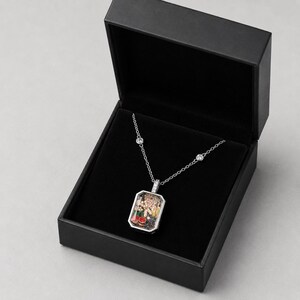 May include: A silver-toned rectangular pendant necklace featuring a clear glass front filled with small, colourful decorative charms including red cherries and yellow flowers, suspended on a delicate chain with two inset clear stones in a black box.