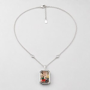 May include: A silver-toned necklace featuring a rectangular pendant filled with small, colourful charms including red cherries, gold-toned shapes, and clear crystals. The chain includes two small circular accents and a lobster clasp closure.