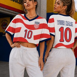 May include: A cropped V-neck jersey featuring a red and white wavy stripe pattern, a dark blue collar, and the number 10 in red on the front. The back displays the text YOUR NAME above the number 10 in red, with dark blue trim on the sleeves.