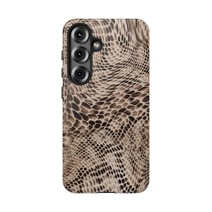 Puede incluir: Funda de teléfono con un diseño de piel de reptil en tonos marrones y beige. La funda tiene un módulo de cámara con tres lentes y un flash. El diseño se asemeja a escamas de serpiente o lagarto, ofreciendo una apariencia texturizada.