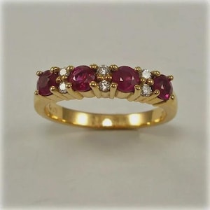 May include: A gold ring featuring five oval-cut rubies and small diamonds. The rubies are a deep red color, and the diamonds are clear and sparkling. The ring has a classic design.