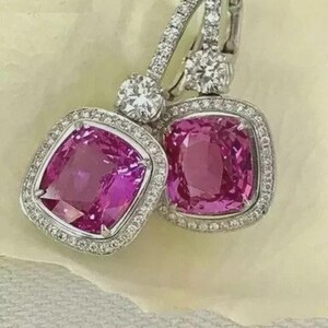 May include: A pair of elegant earrings featuring large, square-cut pink gemstones surrounded by a halo of small, sparkling diamonds. The earrings have a lever-back closure and are set in a silver-colored metal.