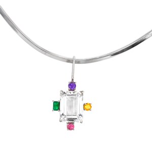 May include: A silver necklace featuring a pendant with a large, rectangular, clear gemstone at its center. The pendant is accented with smaller, colorful gemstones in green, yellow, purple, and pink. The necklace has a simple, curved design.