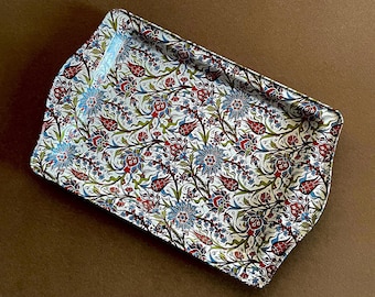 Puede incluir: Una bandeja de servicio rectangular con un patrón floral denso e intrincado de tulipanes y claveles estilizados en tonos rojo, azul y verde sobre un fondo blanco, con una superficie brillante y bordes ligeramente elevados.