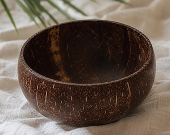 Puede incluir: Un cuenco redondo de coco marrón oscuro con una superficie texturizada. El cuenco tiene un aspecto natural y orgánico, con vetas visibles y rayas de color claro. El cuenco está vacío y se encuentra sobre una superficie blanca y texturizada.