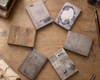 May include: Six rectangular paper pads with vintage-style designs, including ledger sheets, floral frames, and French typography featuring the text HIPPODROME BAL, arranged in a circular pattern on a wooden surface with an inkwell and paper clip.