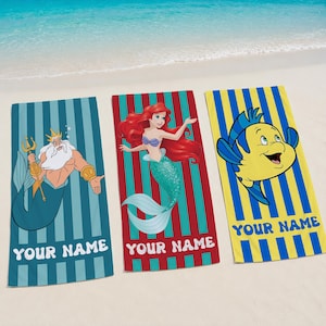 May include: Three beach towels with cartoon characters and the text "YOUR NAME". One towel features a teal background with a cartoon of King Triton. Another has a red background with Ariel. The third has a yellow background with Flounder.