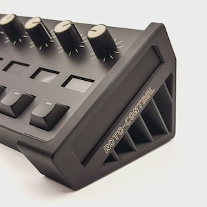 Könnte beinhalten: Ein schwarzes elektronisches Bedienfeld mit Knöpfen, Drehreglern und dem Text "ROTO-CONTROL" in Weiß. Das Panel hat eine Reihe von Knöpfen mit weißen Markierungen und mehrere rechteckige Tasten. Die Seite des Panels weist ein geometrisches Design auf.