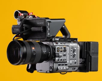 May include: A professional-grade Sony FX6 cinema camera with a large lens, mounted accessories, and a matte black finish. The camera is set against a bright yellow background, showcasing its sleek design and advanced features.