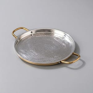 May include: A round metal serving tray with a hammered silver interior and a gold-colored rim and handles. The tray is approximately 12 inches in diameter and is designed for serving food or displaying items.
