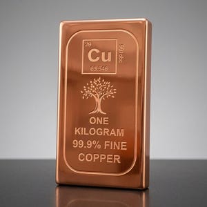Könnte beinhalten: Ein rechteckiger Kupferbarren mit polierter Oberfläche. Der Barren zeigt das chemische Symbol Cu, die Ordnungszahl 29 und den Text "ONE KILOGRAM 99.9% FINE COPPER". Ein Baumdesign ist ebenfalls vorhanden.