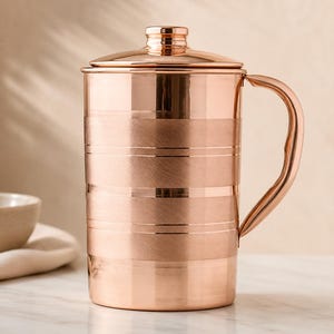 May include: A cylindrical copper pitcher with a polished finish and a matching lid. The body features alternating bands of smooth, reflective copper and textured, brushed horizontal stripes. It includes a curved handle on the right side.