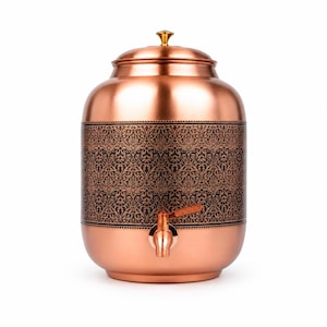 May include: A cylindrical copper water dispenser featuring a polished metallic finish and a central band decorated with a dark, intricate floral pattern. The vessel includes a matching copper lid with a small gold-toned knob and a copper spigot.
