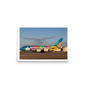 May include: A large passenger aircraft with a vibrant design and the text "BE PART OF THE MAGIC" on its side. The plane is painted in blue, red, yellow, and orange, set against a blue sky.