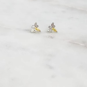 May include: A pair of silver-toned stud earrings shaped like bees. Each earring features clear, sparkling stones along the wings and a single yellow, marquise-cut stone forming the body of the bee, creating a delicate and detailed insect design.