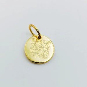 May include: A gold-coloured, round pendant with a small loop at the top. The pendant features a QR code design with the Instagram logo. The pendant is made of a shiny, reflective metal.