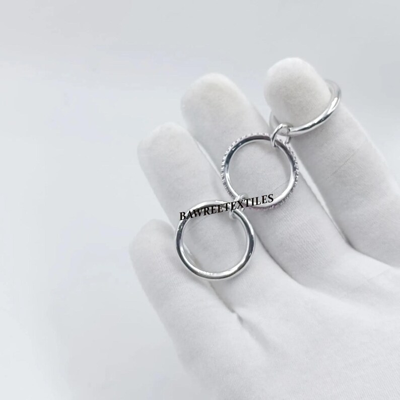 Pu&ograve; includere: Un anello color argento con tre cerchi interconnessi. Un cerchio &egrave; adornato con piccole pietre scintillanti. Il testo "BAWREETEXTILES" &egrave; visibile sull'anello. L'anello &egrave; presentato su sfondo bianco.