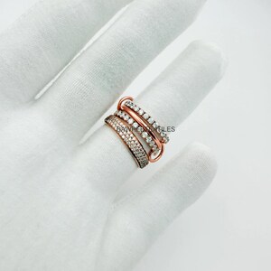 Op de afbeelding: Een roségouden ring met vier banden, elk bezet met kleine, heldere edelstenen. De banden zijn gestapeld en verbonden, waardoor een gelaagd effect ontstaat. De ring wordt gepresenteerd op een witte ondergrond.