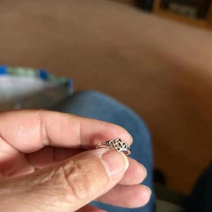 以下が含まれることがあります： ケルトノットのデザインが施されたシルバーカラーのリング。リングは手で持たれており、ノットワークの複雑なディテールが示されています。リングのバンドは細く、ノットが焦点となっています。