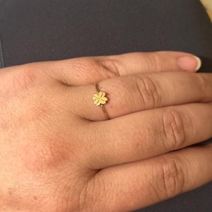 Könnte beinhalten: Ein goldfarbener Ring mit einem vierblättrigen Kleeblatt-Design. Der Ring ist dünn und zart, wobei das Kleeblatt im Mittelpunkt steht. Der Ring wird an einem Finger getragen und unterstreicht die schlichte Eleganz des Schmucks.