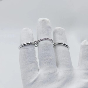 Pu&ograve; includere: Un set di anelli d'argento, uno con una delicata fascia di piccole pietre rosa, collegato a un secondo anello d'argento liscio da una barra curva. La barra &egrave; incisa con la scritta "BAUBLE TEXTILES".