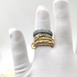 Op de afbeelding: Een verzameling ringen in zilver- en goudtinten, sommige bezet met kleine, sprankelende stenen. De ringen zijn op een vinger gestapeld en tonen hun verschillende ontwerpen en texturen. Op een witte achtergrond.