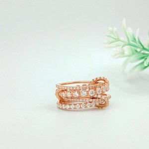 Può includere: Anello in oro rosa con più fasce, ciascuna incastonata con piccole gemme trasparenti. L'anello ha un design a strati, con le fasce leggermente sfalsate. Le gemme brillano sull'oro rosa.