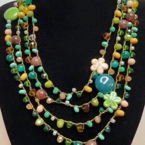Può includere: Collana a più fili con una varietà di perline colorate nelle tonalità del verde, giallo, rosa e marrone. La collana presenta perline grandi e arrotondate e accenti floreali. La collana è esposta su un manichino nero.