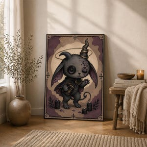 May include: A framed rectangular wall art print featuring a dark grey, horned creature with one button eye and one closed eye, wearing a cape and holding a book. The illustration includes a halo, three black candles, and purple accents.
