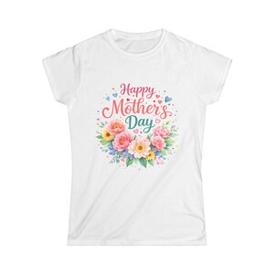 Può includere: T-shirt bianca con un design floreale e la scritta "Happy Mother's Day". Il design presenta fiori rosa, gialli e blu disposti a cerchio, con piccoli cuori e punti che circondano il testo.