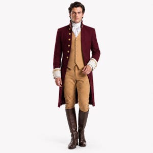 Peut inclure: Un long manteau bordeaux avec des boutons dorés et des poignets blancs, porté sur un gilet beige et un pantalon beige assorti. La tenue comprend une chemise blanche à col avec une cravate et des bottes en cuir marron foncé montant au genou.