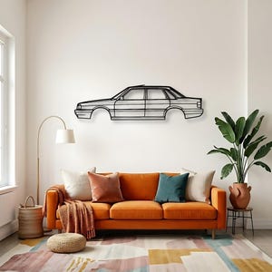 Puede incluir: Una pieza de arte mural de metal negro que representa el contorno de un coche clásico. La obra de arte está montada en una pared blanca sobre un sofá naranja con cojines coloridos y una alfombra estampada. Una lámpara de pie y plantas en macetas completan la decoración.
